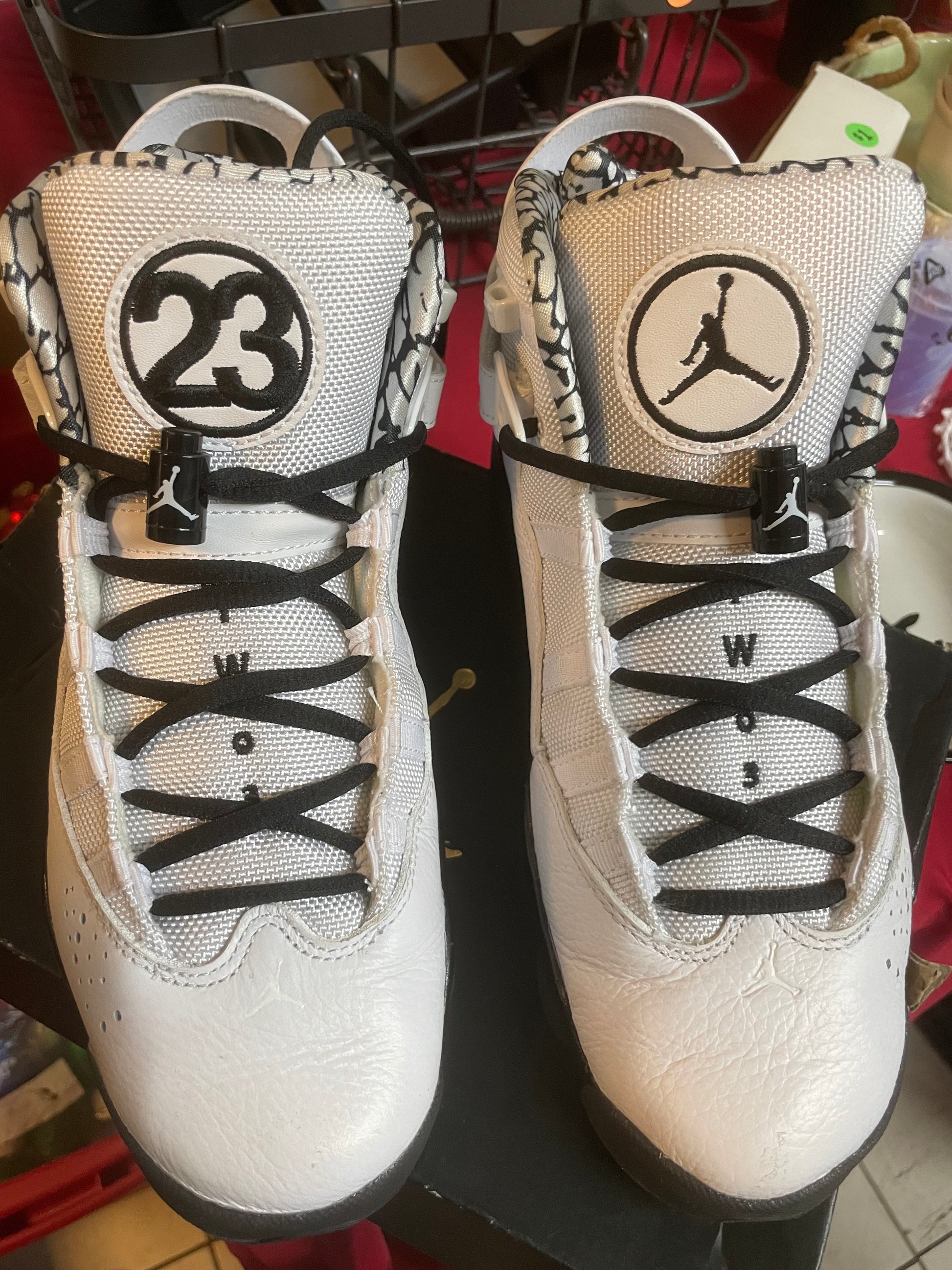 Pair of white sneakers with black laces and logos on a dark surface.